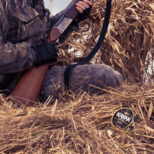 Hunter crouched waiting in blind with gun - Kayak can in hand.