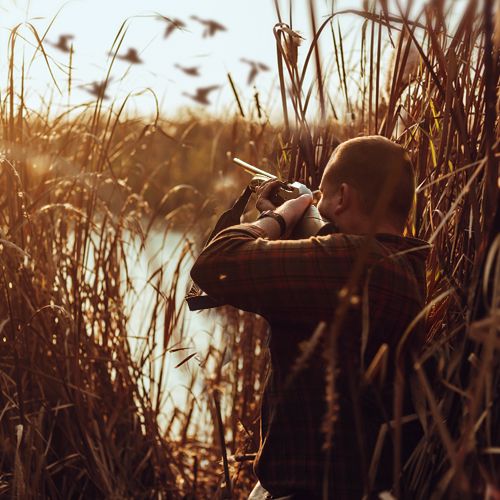 Hunter with shotgun pointed into the sky taking a shot at a duck.